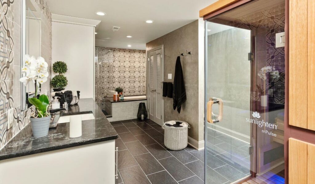 Luxury spa bathroom with dark tile flooring, dark marble countertops, white custom cabinetry and a sauna