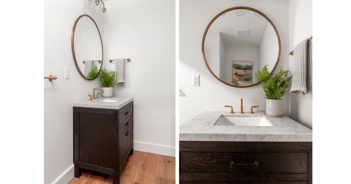 Powder room with dark wood vanity, gold round mirror and marble countertop.