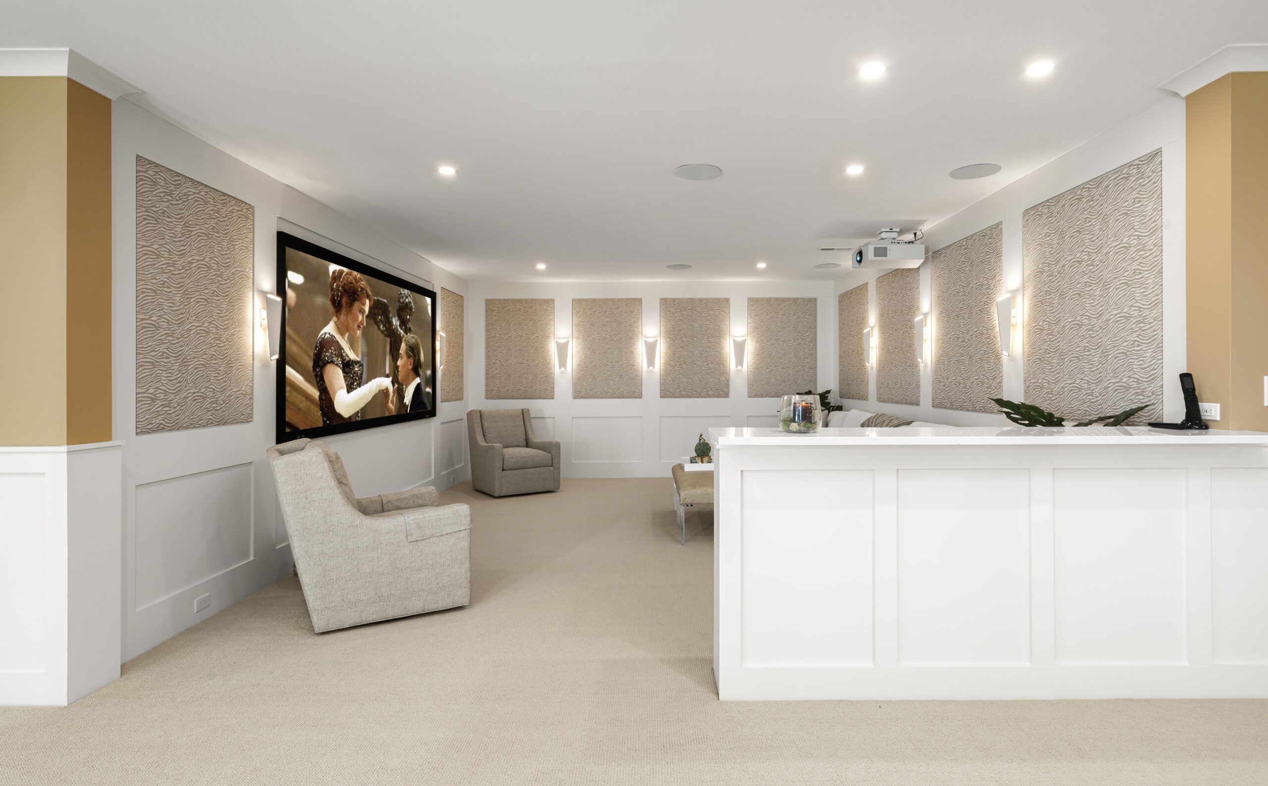 View of theater room with half wall, sconces and beige walls.